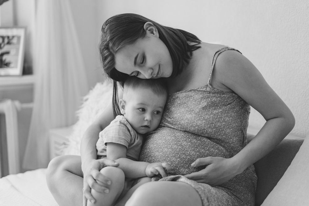 A pregnant woman is sitting on a bed holding a baby.