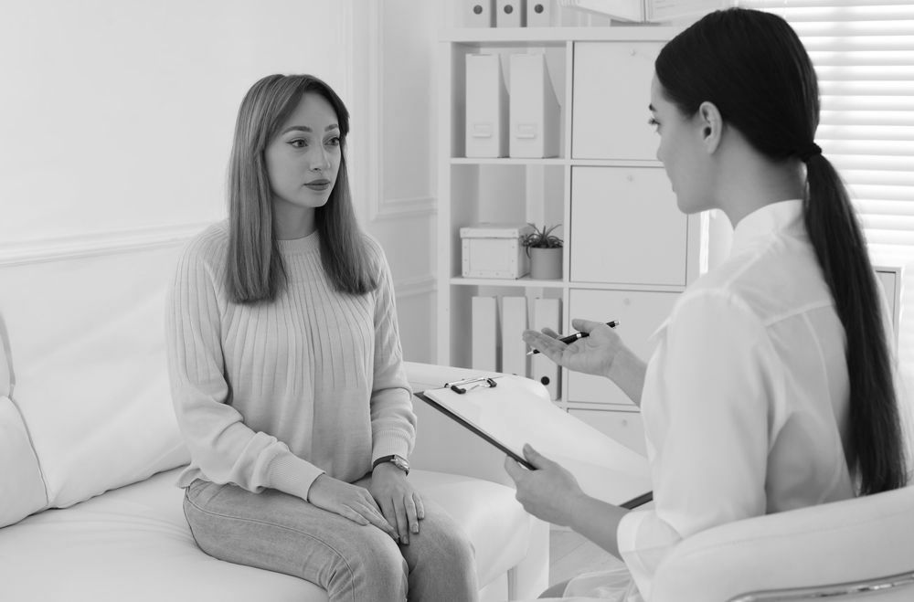 A woman is sitting on a couch talking to a doctor.