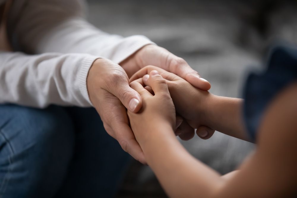 A woman is holding a child 's hand while sitting on a couch.