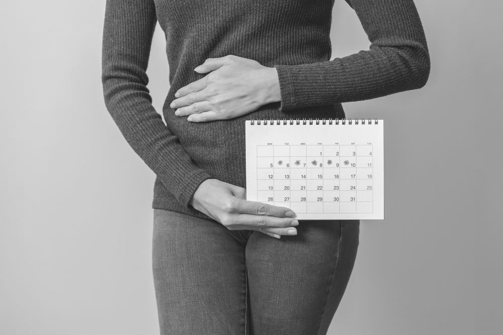 Woman holding a calendar with circled dates, hand on abdomen.