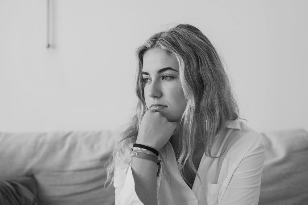 A woman is sitting on a couch with her hand on her chin.