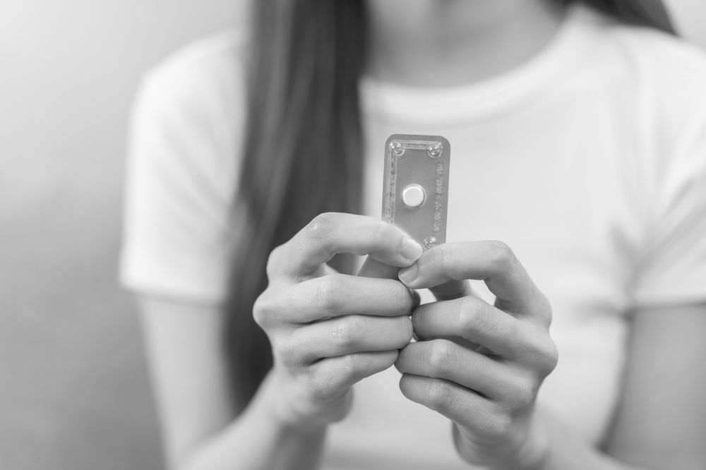 A woman is holding a pill in her hands in a black and white photo.