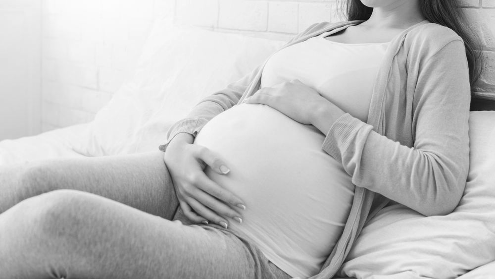 A pregnant woman is sitting on a bed holding her belly.