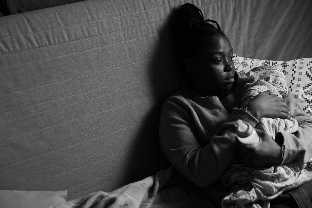 A woman cradles an infant, resting on a bed..