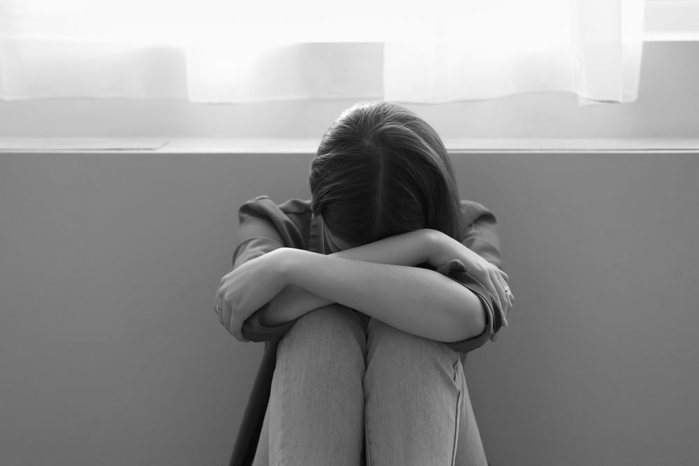 A woman is sitting on the floor with her head down.