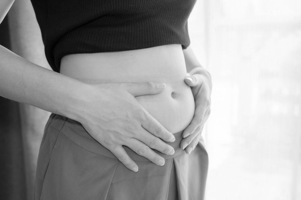 Person's hands touching their abdomen, wearing a black crop top and high-waisted pants.