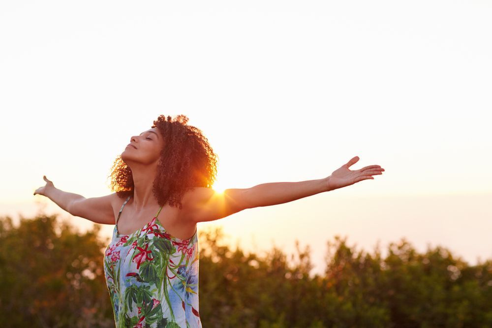 A woman is standing in a field with her arms outstretched at sunset.