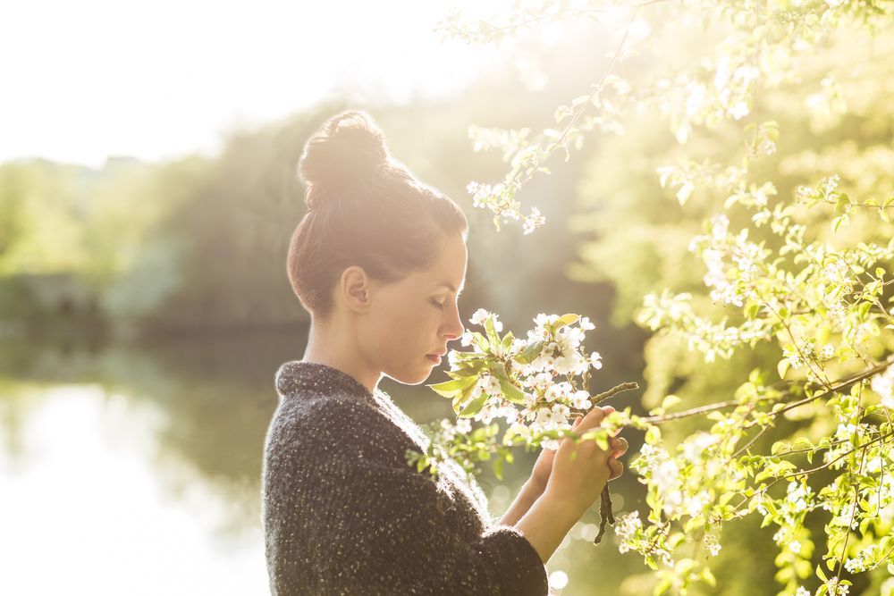 A woman is smelling flowers on a tree branch.