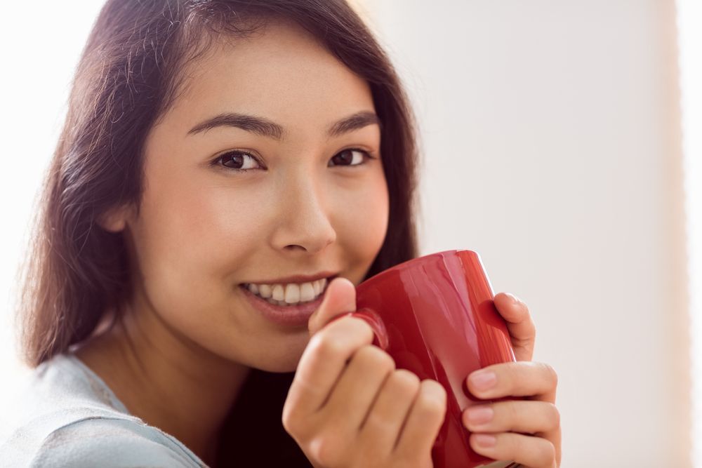 A woman is holding a red cup of coffee and smiling.