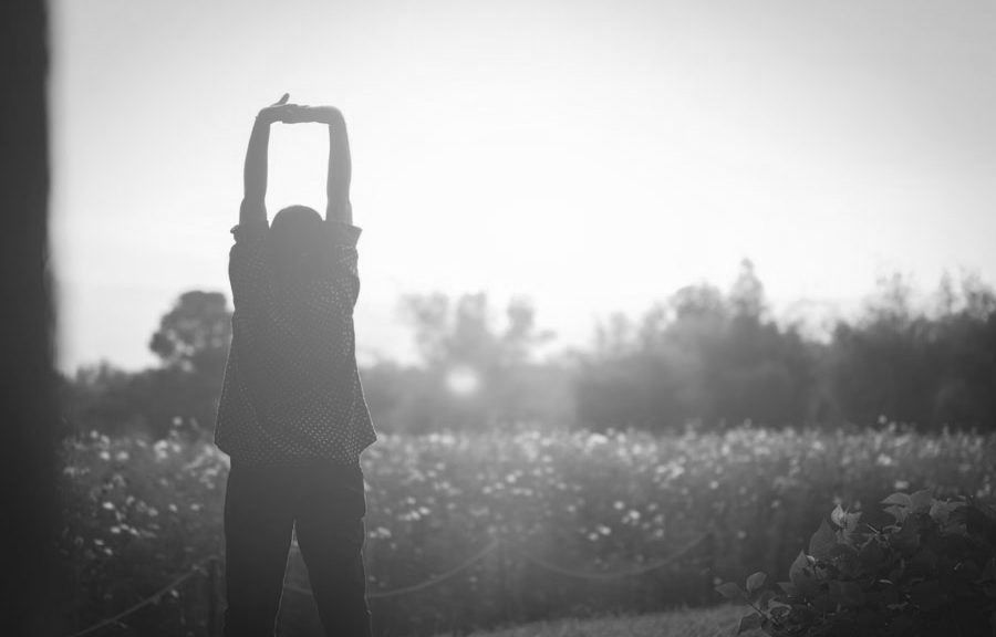 A woman is stretching her arms in a field of flowers at sunset.