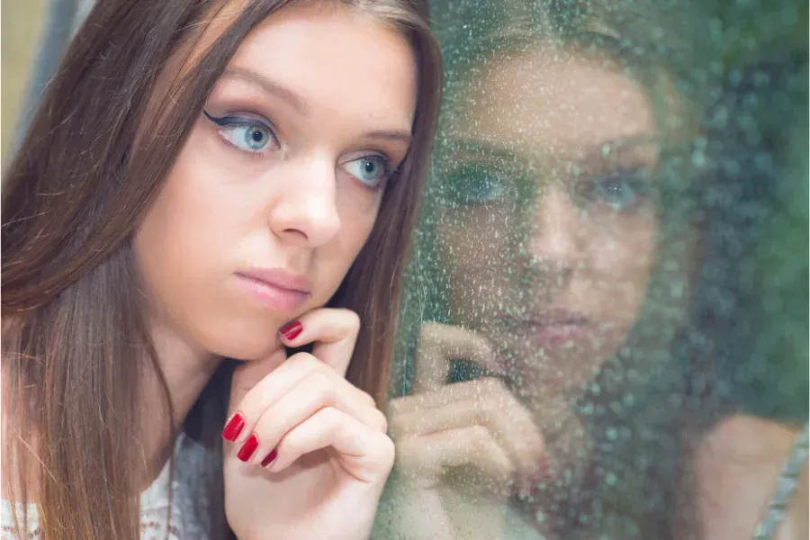 A woman is looking out of a window at her reflection.