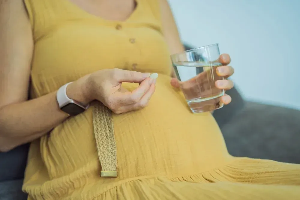 A pregnant woman is taking a pill and holding a glass of water.