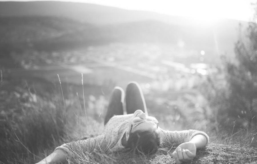 A woman is laying in the grass on top of a hill.