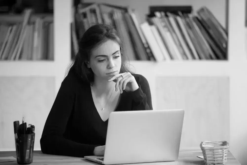 A woman is sitting at a desk using a laptop computer.