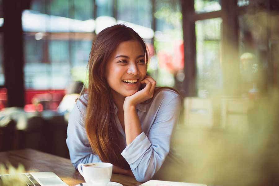 A woman is sitting at a table with a cup of coffee and smiling.