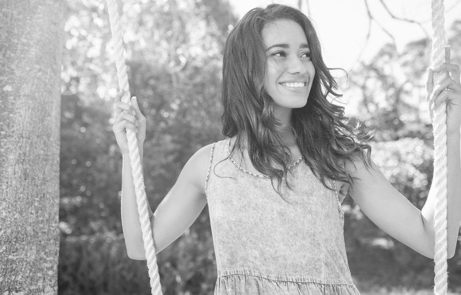 A woman is smiling while sitting on a rope swing.