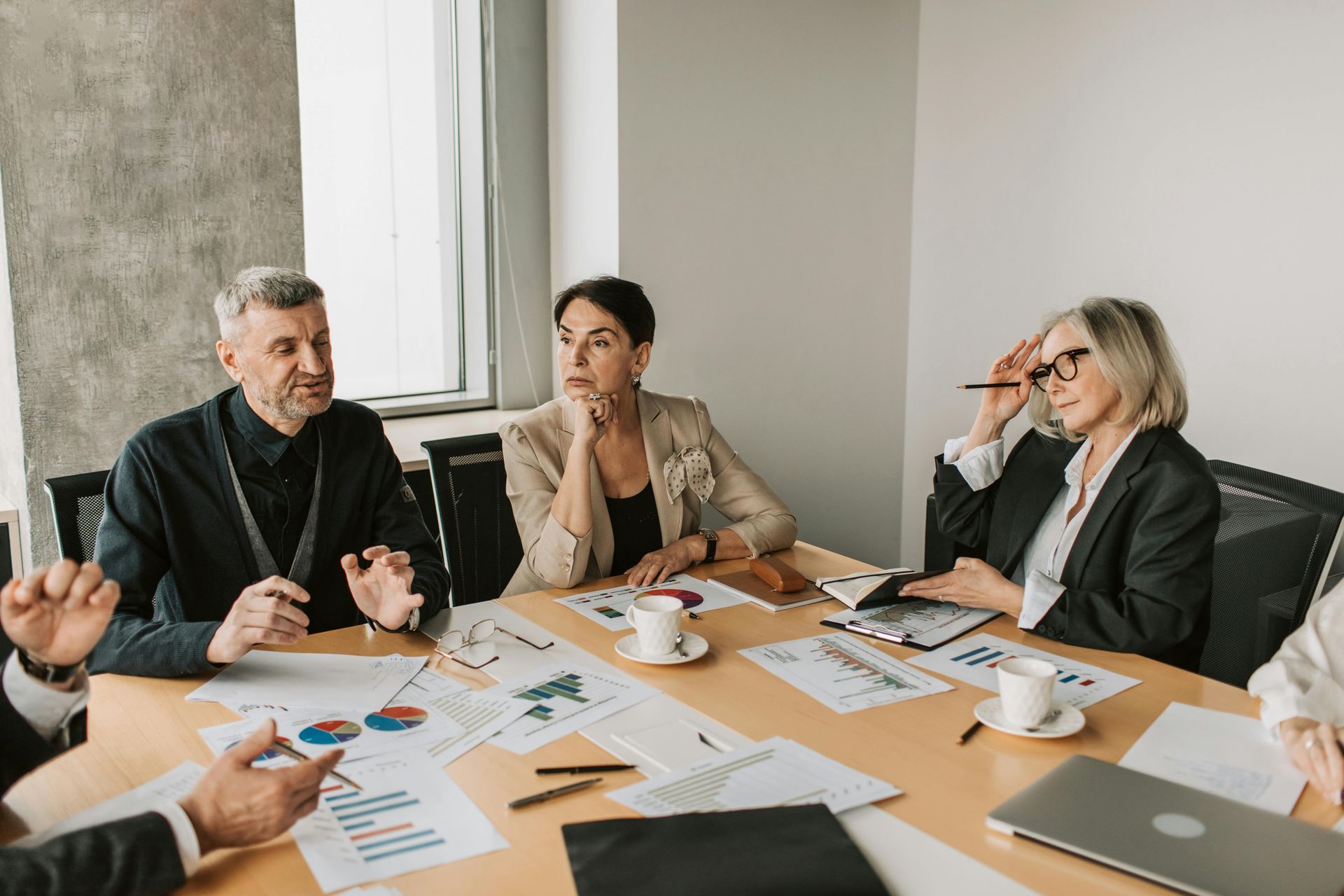 A business meeting in a bright office where four professionals discuss charts and documents spread across a table.