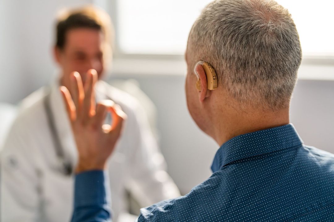 Un uomo con un apparecchio acustico sta parlando con un medico.