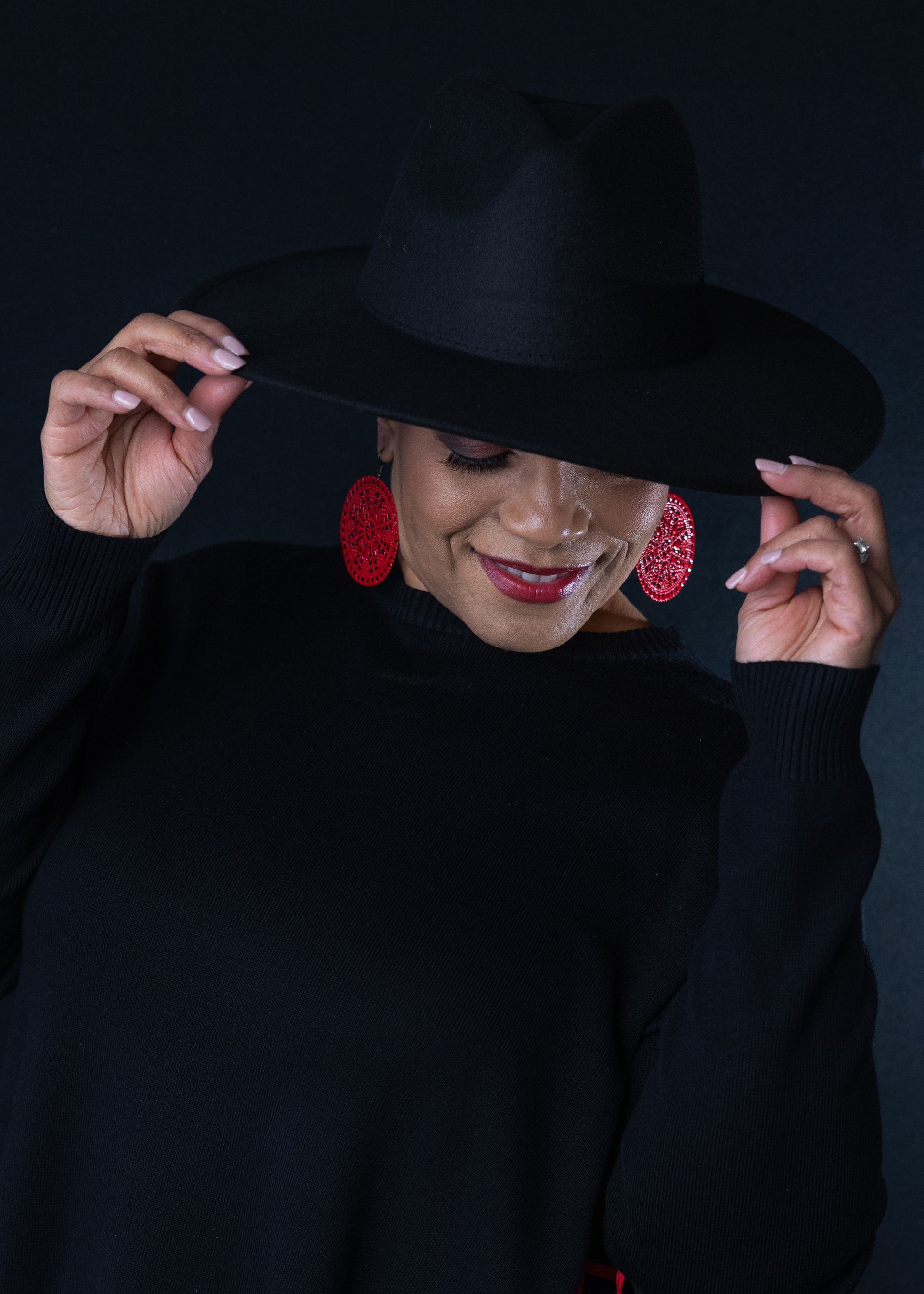 A woman wearing a black hat and red earrings is smiling.