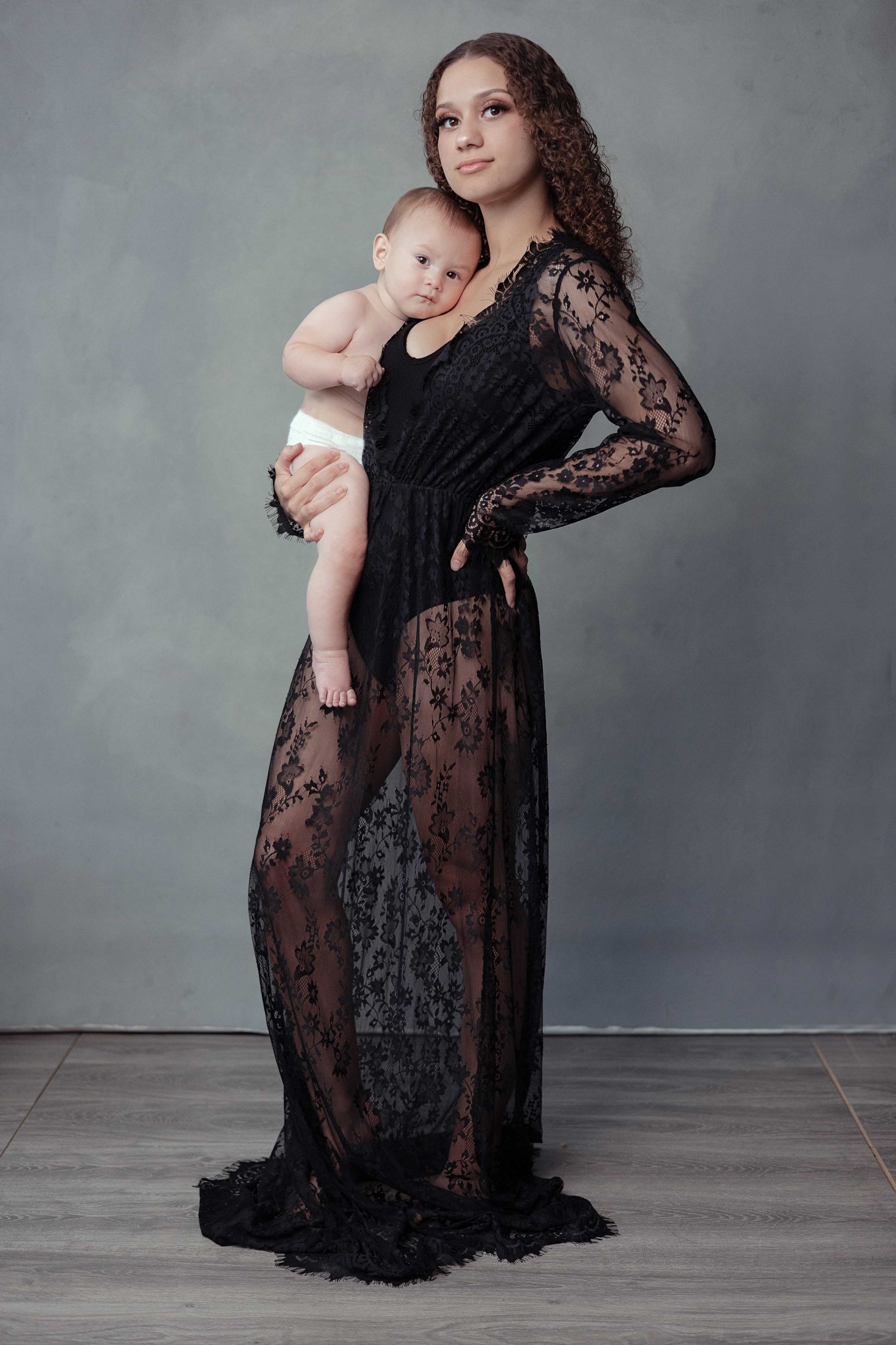 A woman in a black lace dress is holding a baby.