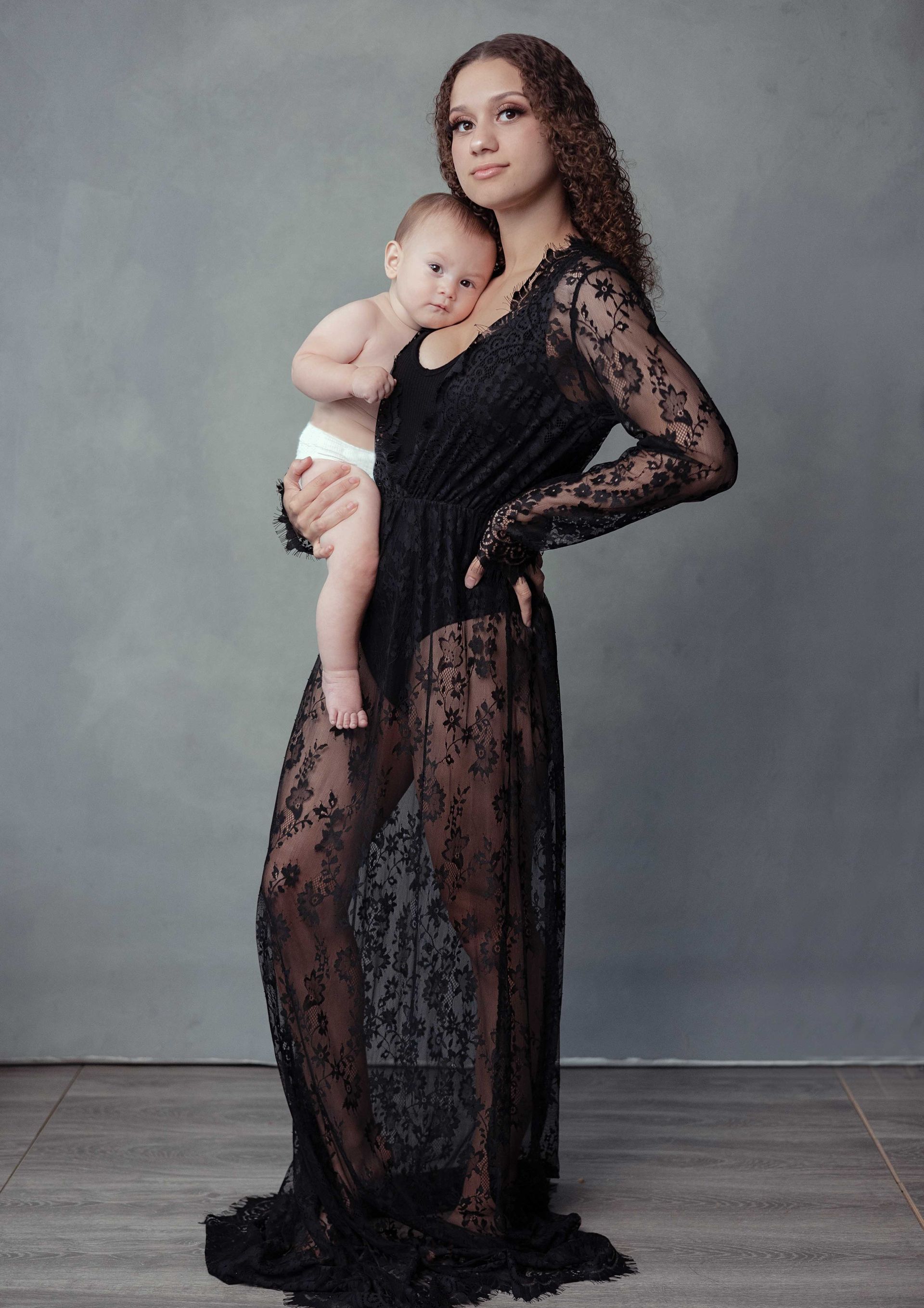 A woman in a black lace dress is holding a baby.