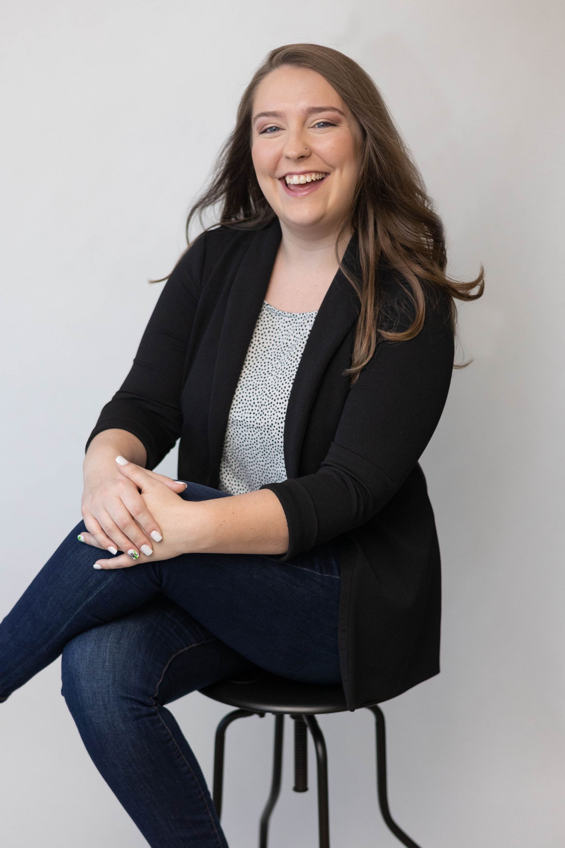 A woman is sitting on a stool with her legs crossed and smiling.