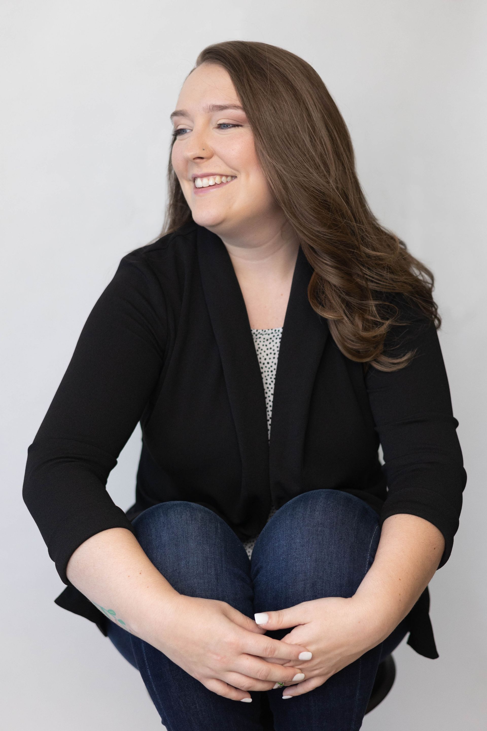 A woman is sitting on a stool with her legs crossed and smiling.