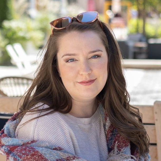 A woman wearing sunglasses and a scarf is sitting on a bench.