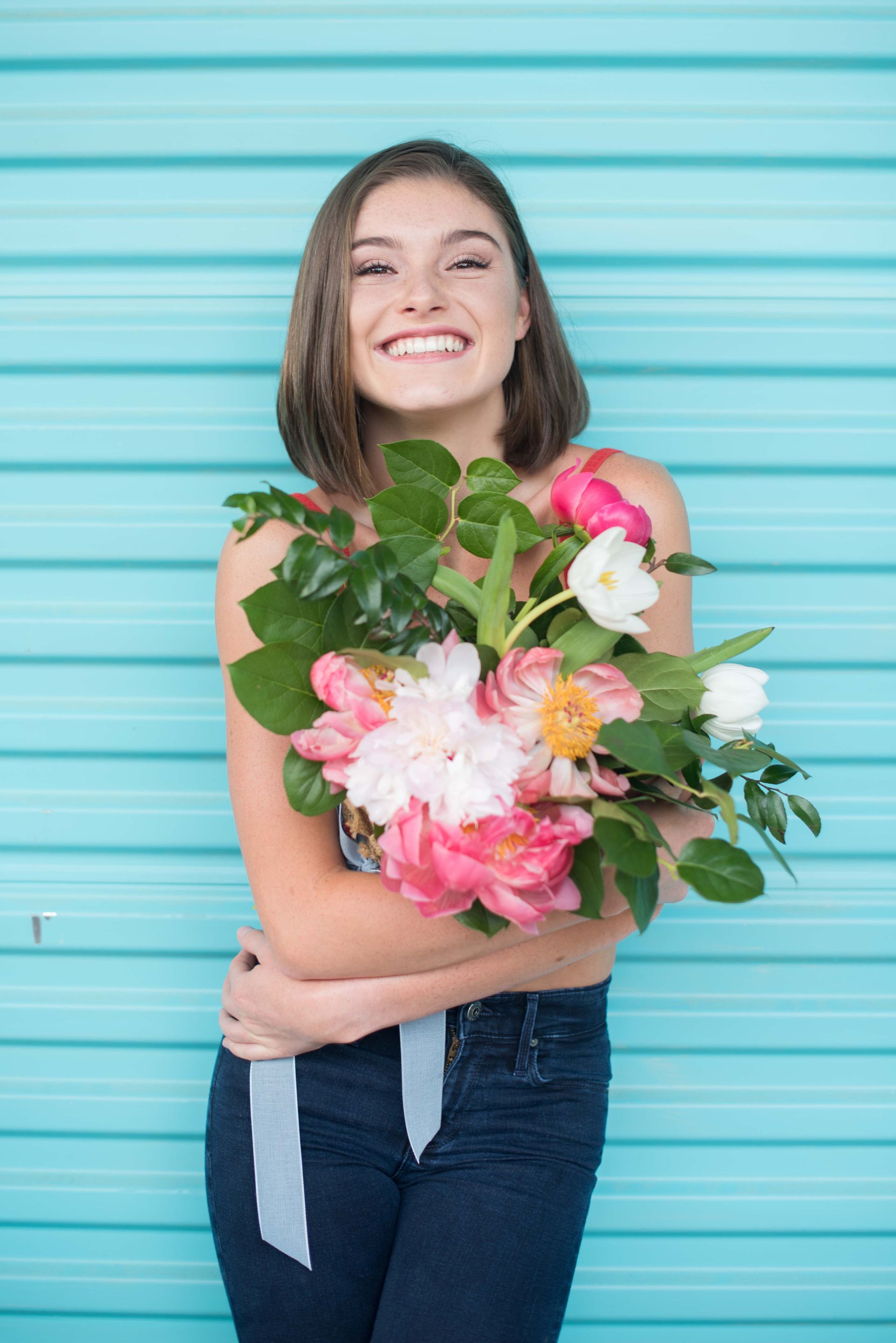 A woman is holding a bouquet of flowers in front of a blue wall.