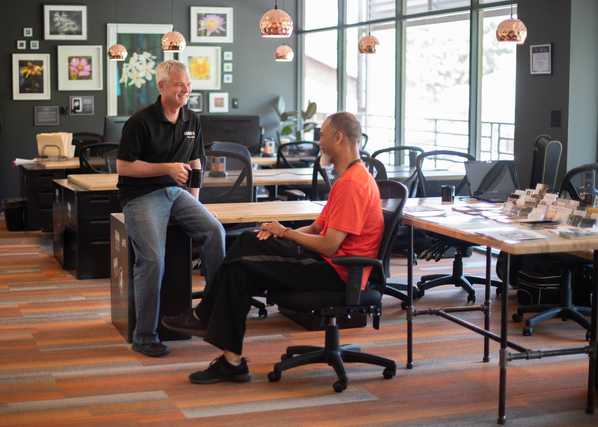 Two men are sitting at desks in an office talking to each other.