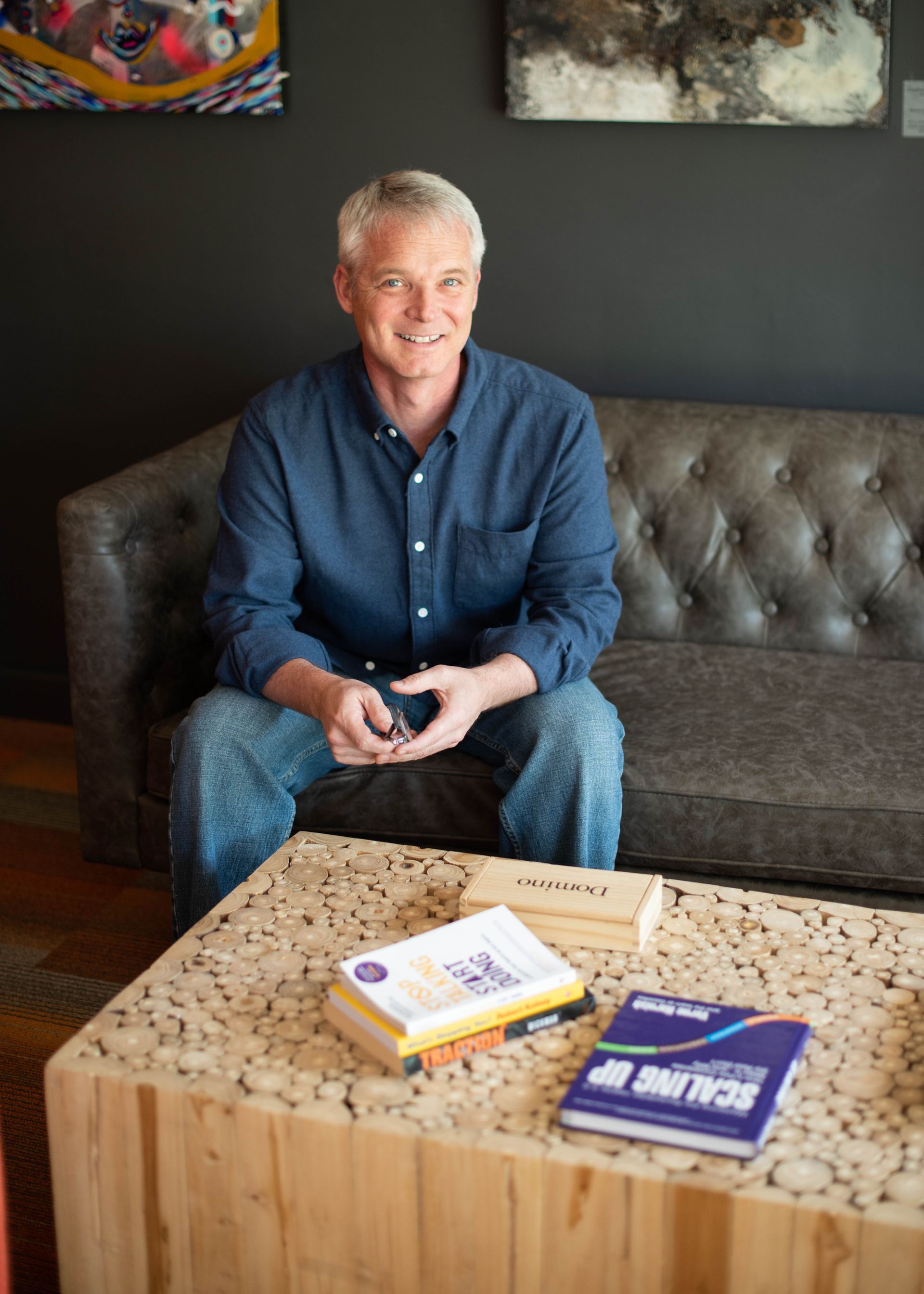 A man is sitting on a couch next to a table with books on it.