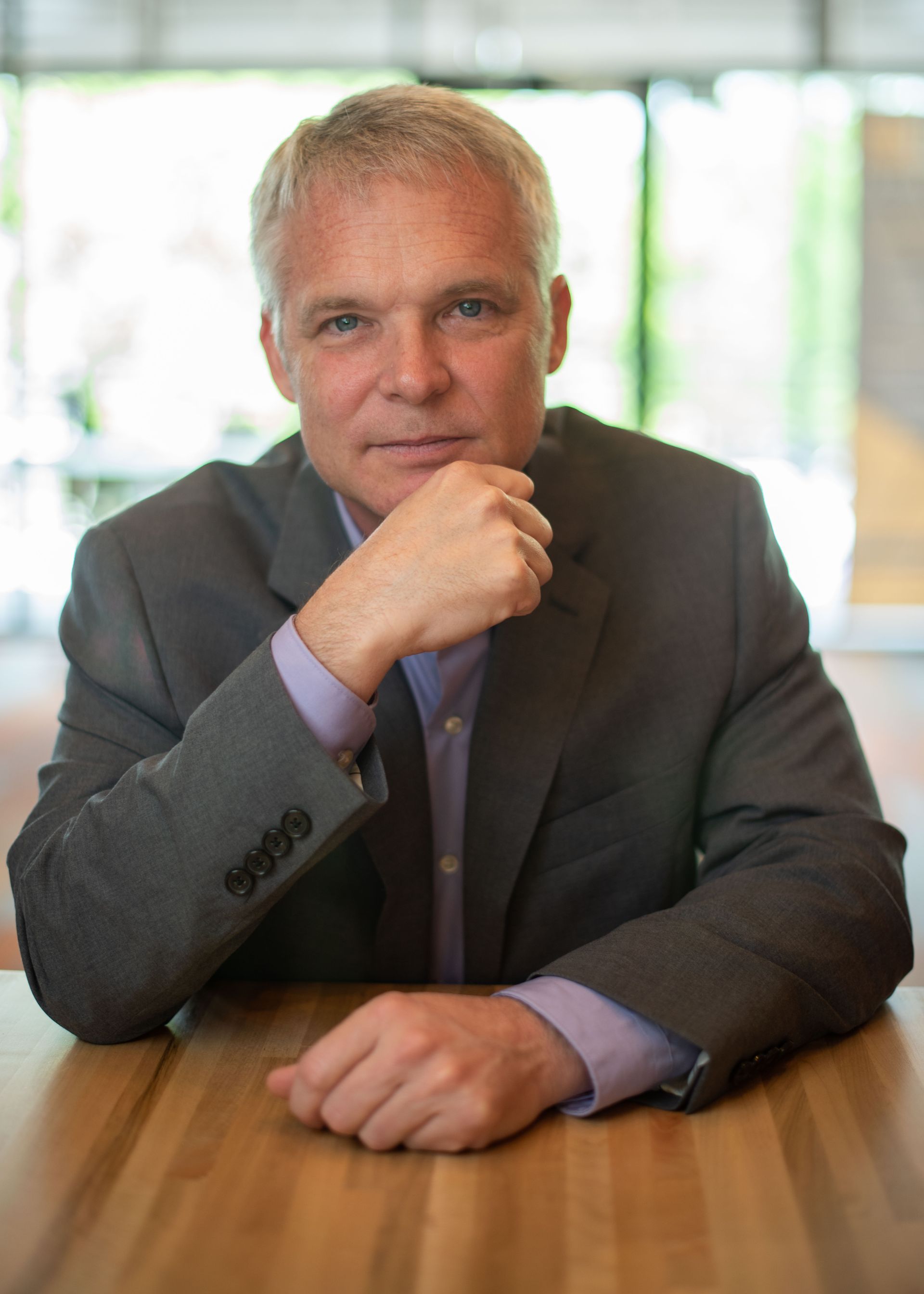 A man in a suit is sitting at a table with his hand on his chin.