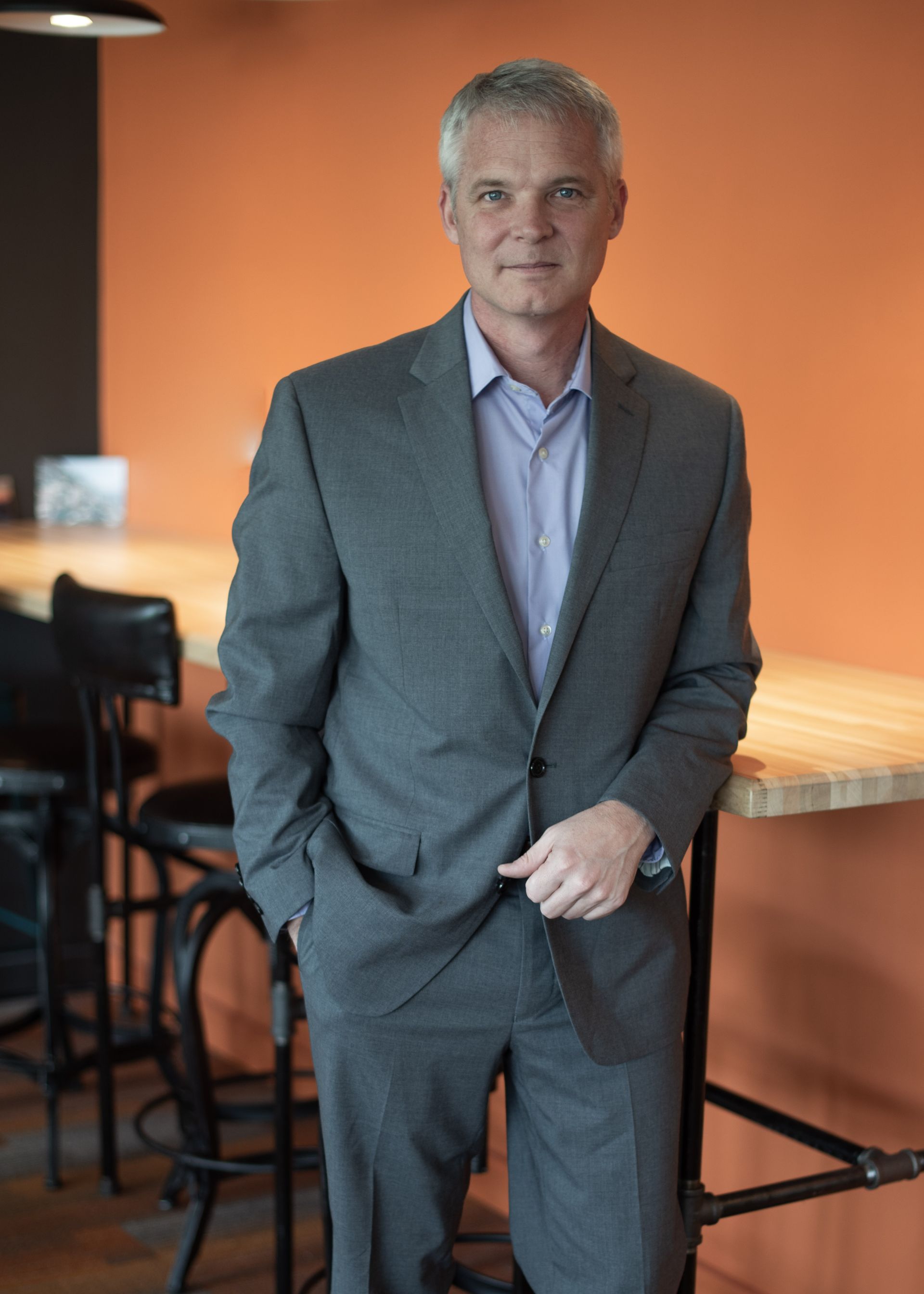 A man in a suit is standing in front of a table with his hands in his pockets.