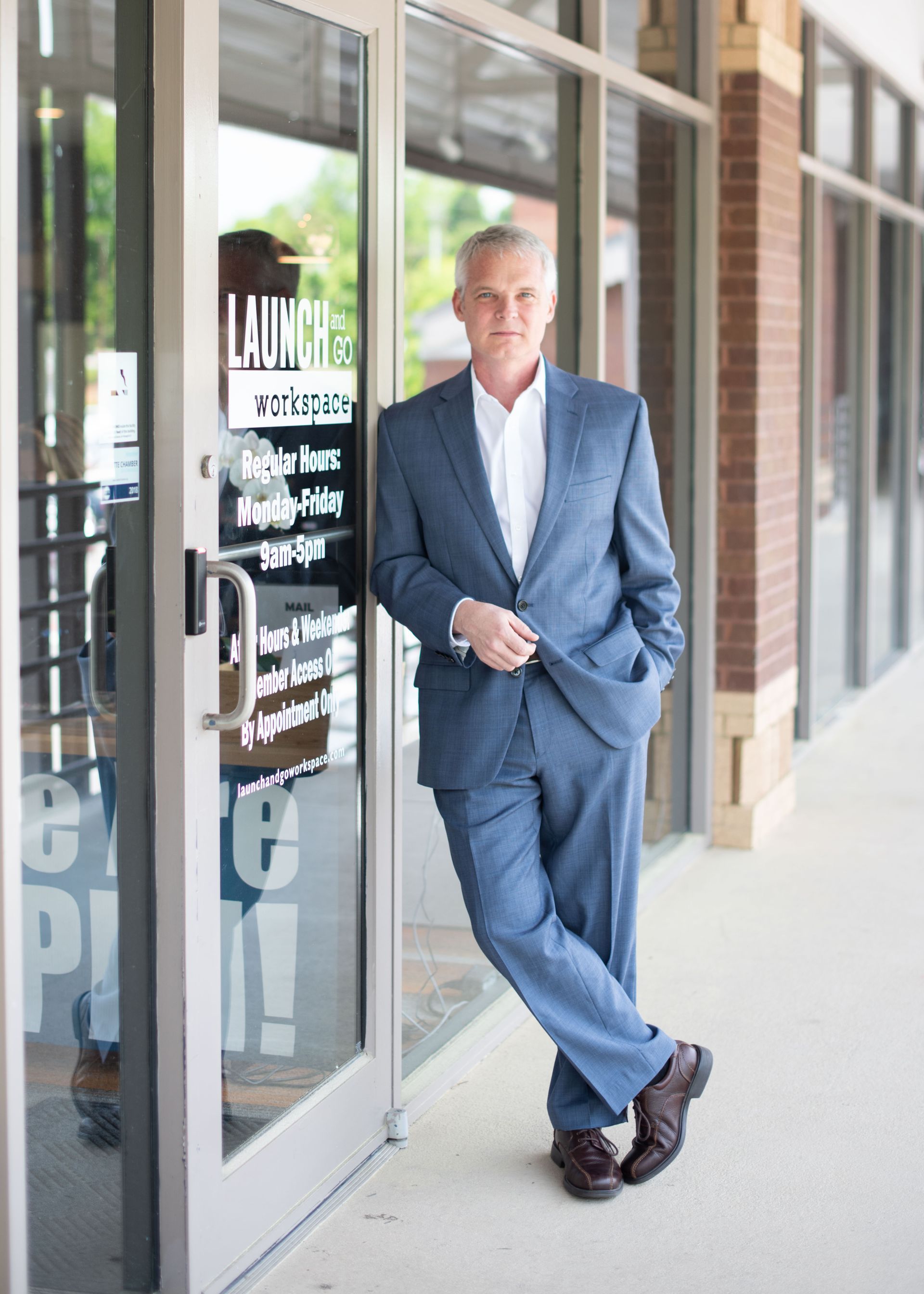 A man in a suit is leaning against a glass door.