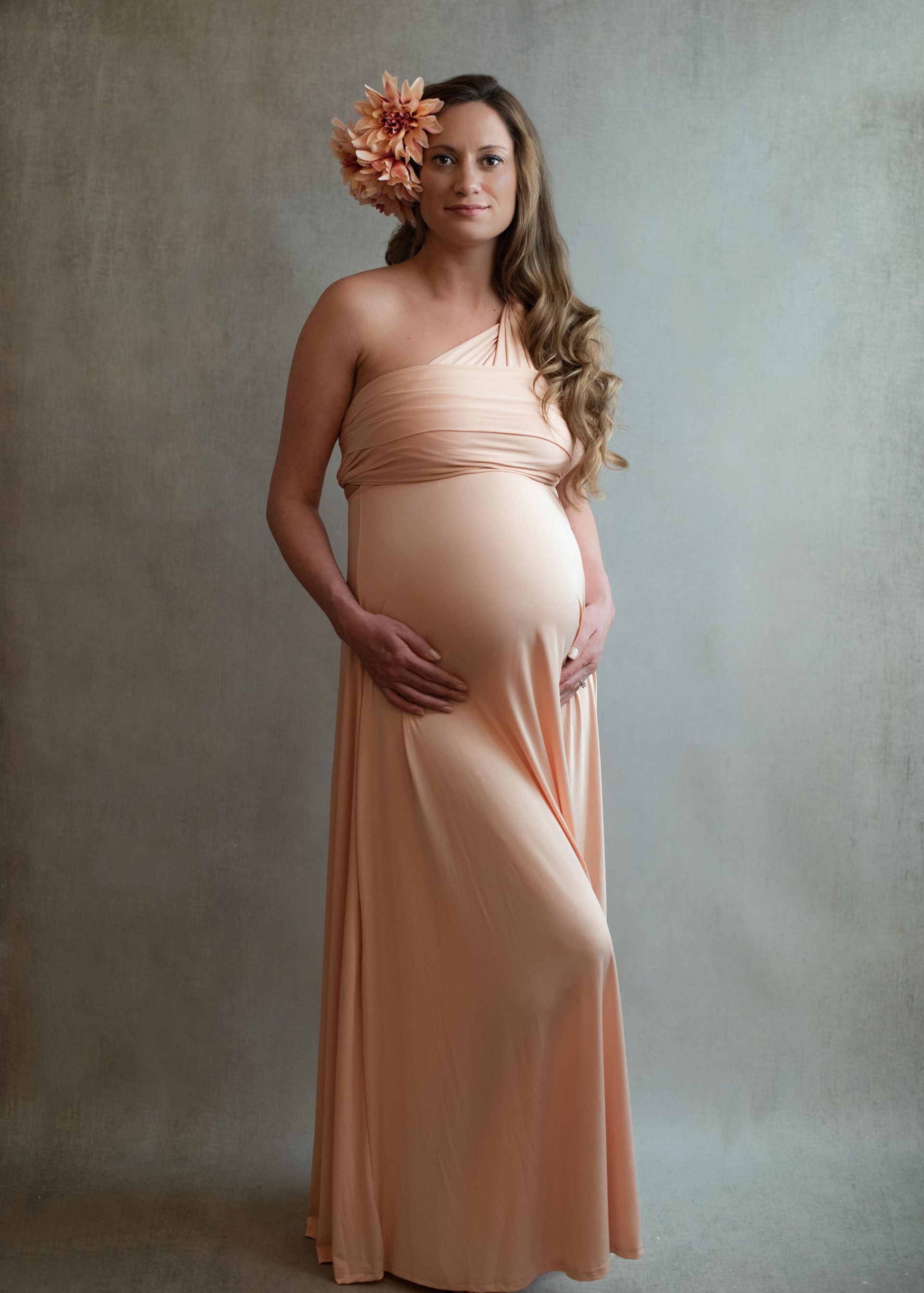 A pregnant woman in a long peach dress with a flower in her hair.