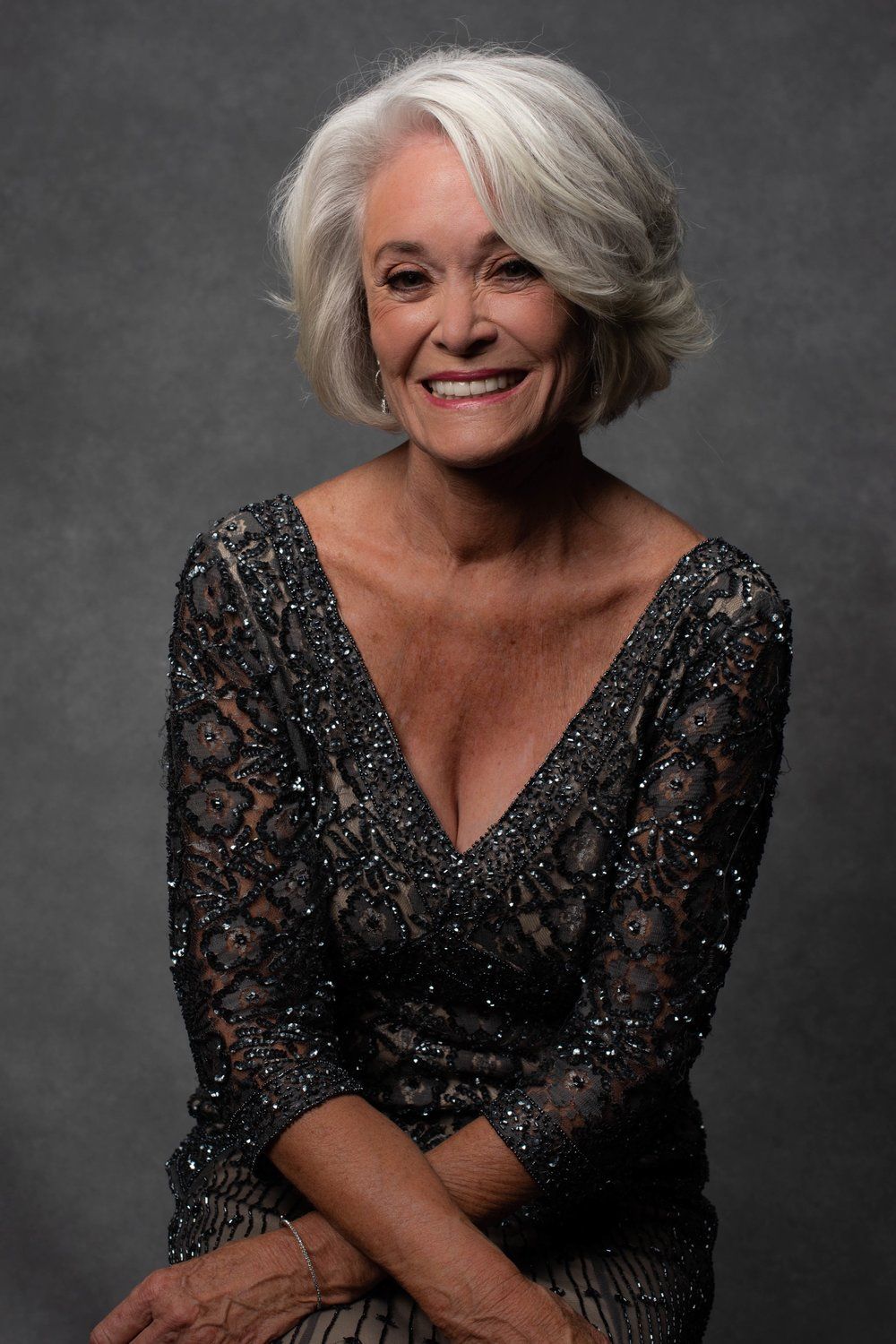 A woman with gray hair is wearing a black dress and smiling.