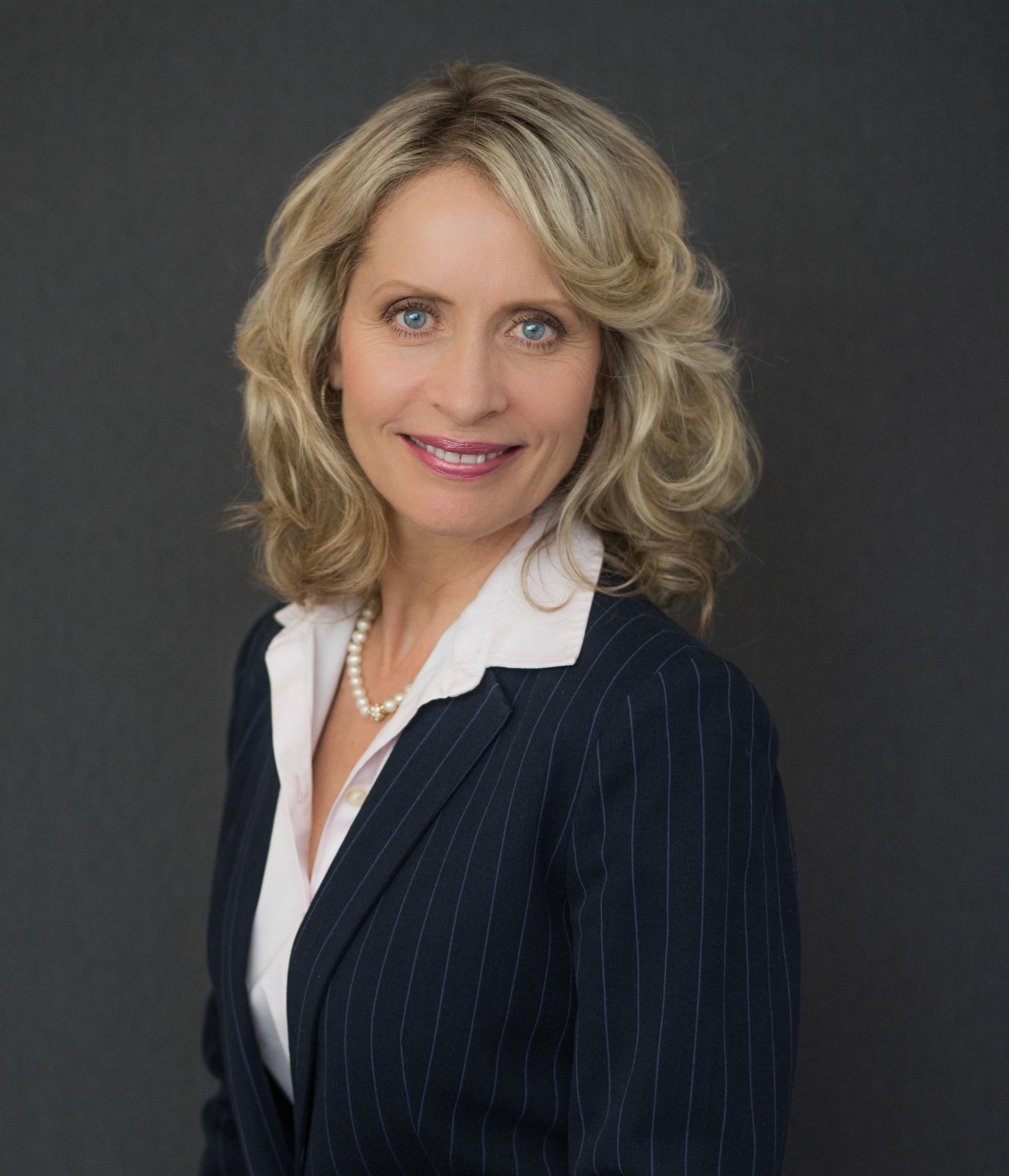 A woman in a suit and white shirt is smiling for the camera.