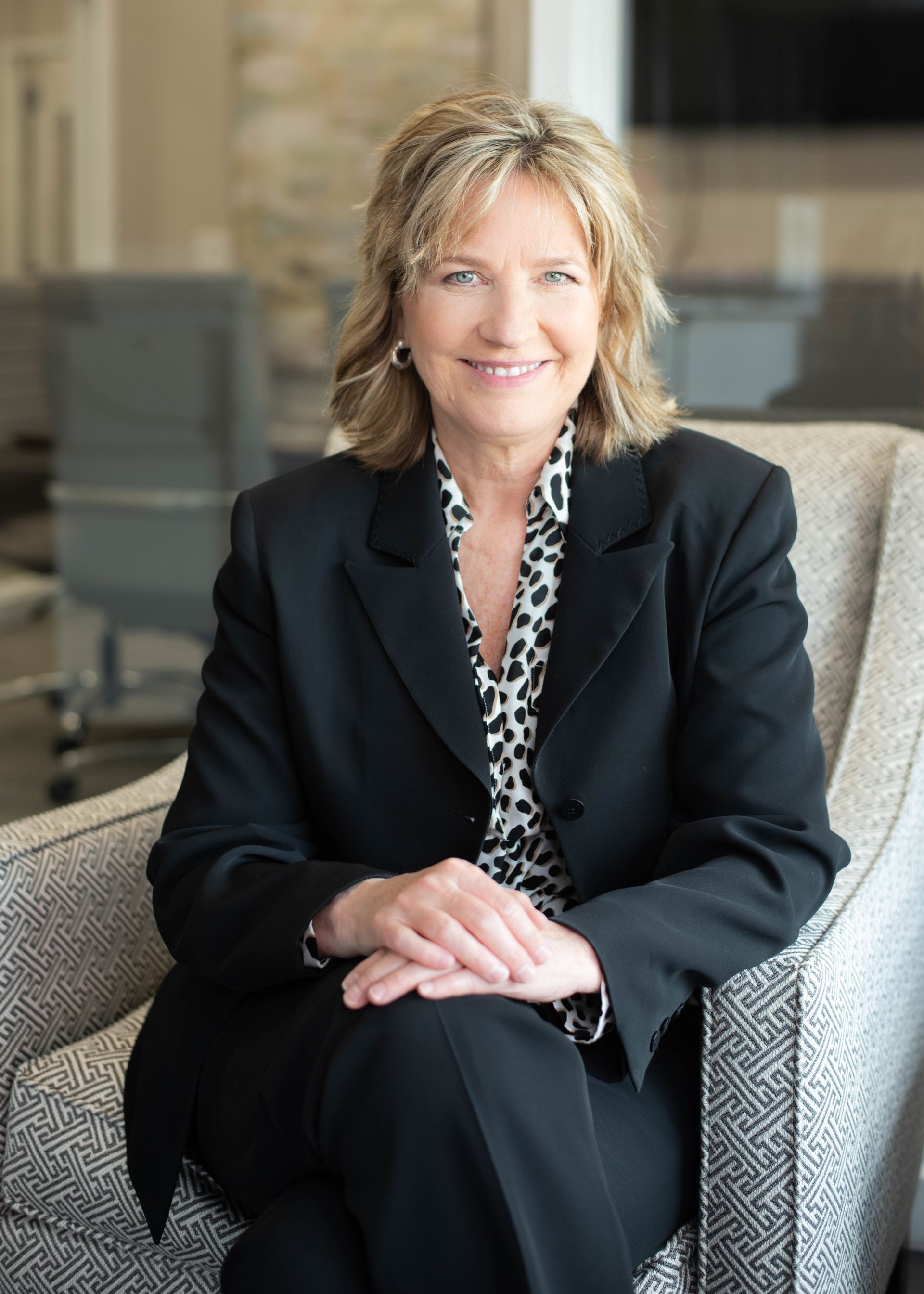 A woman in a suit is sitting in a chair with her legs crossed.