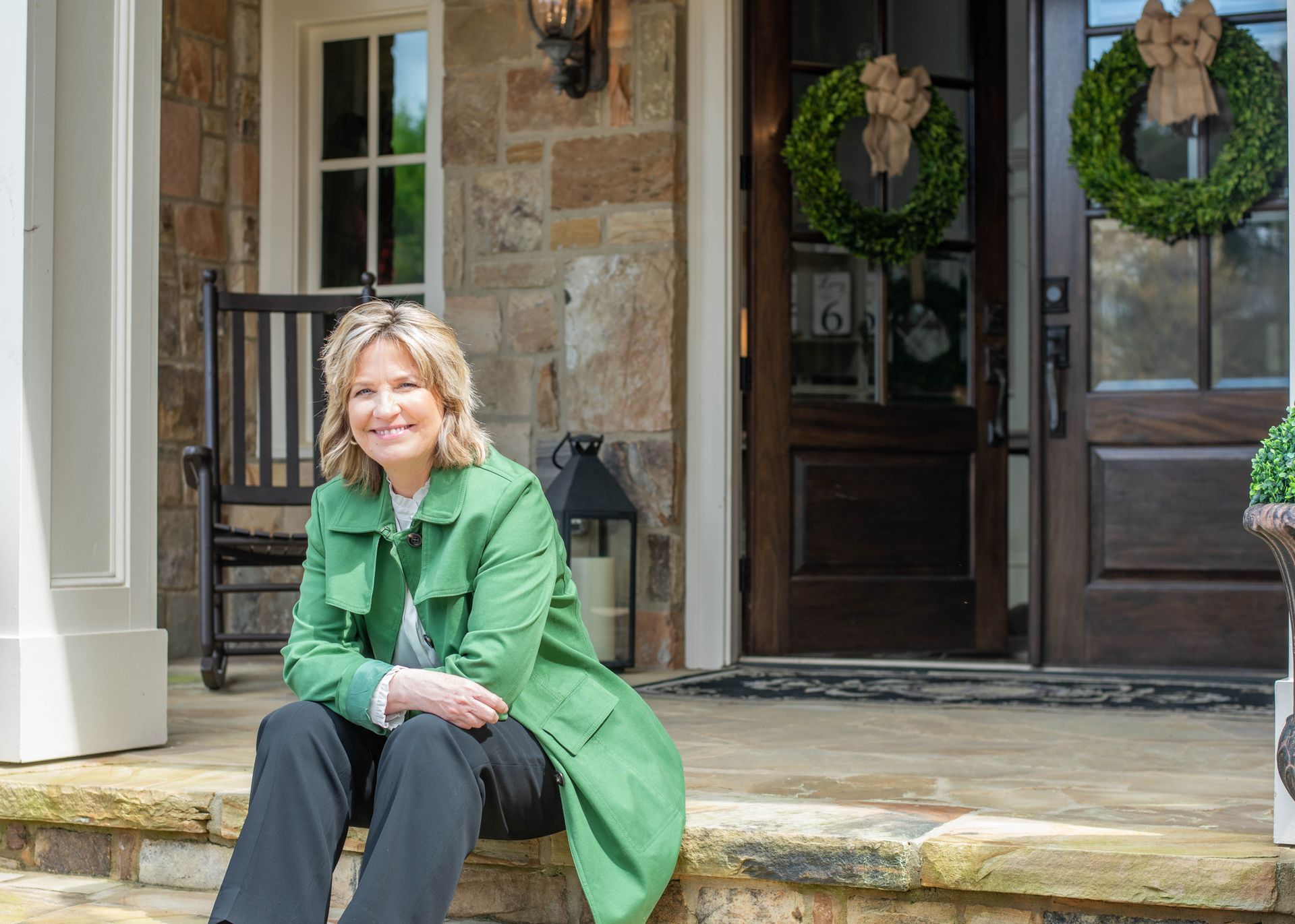 A woman in a green coat is sitting on the steps of a house.