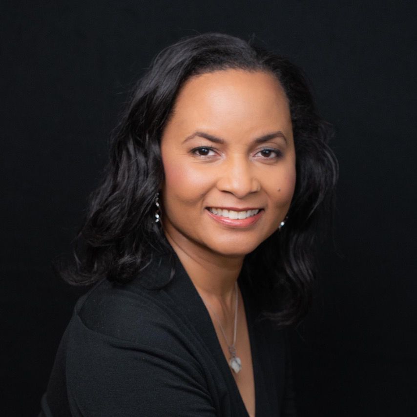 A woman in a black jacket and necklace is smiling for the camera.