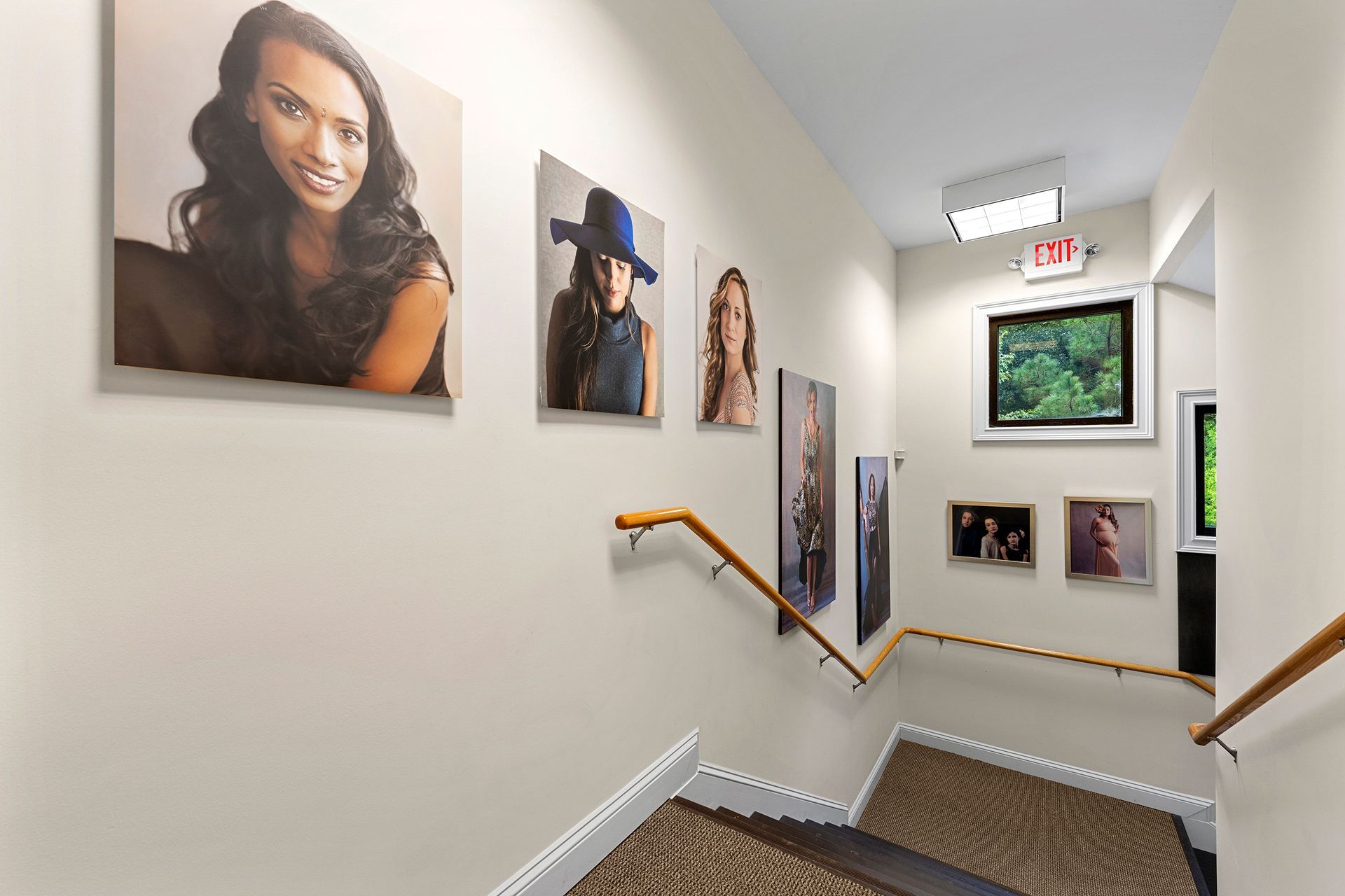 A staircase with pictures on the wall and a red exit sign.