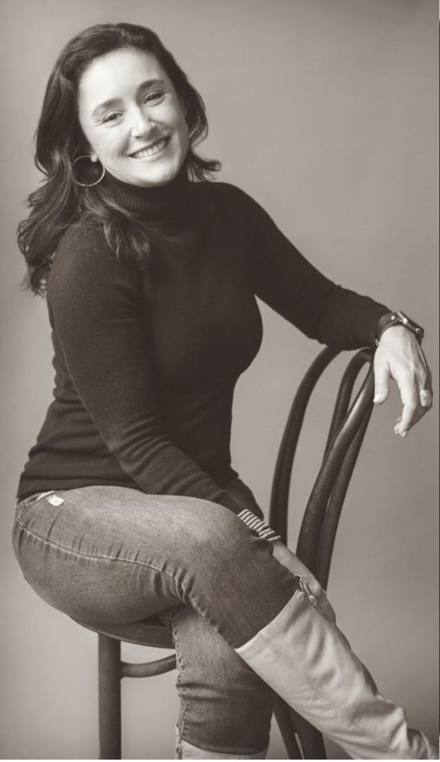 A black and white photo of a woman smiling with her arms crossed.