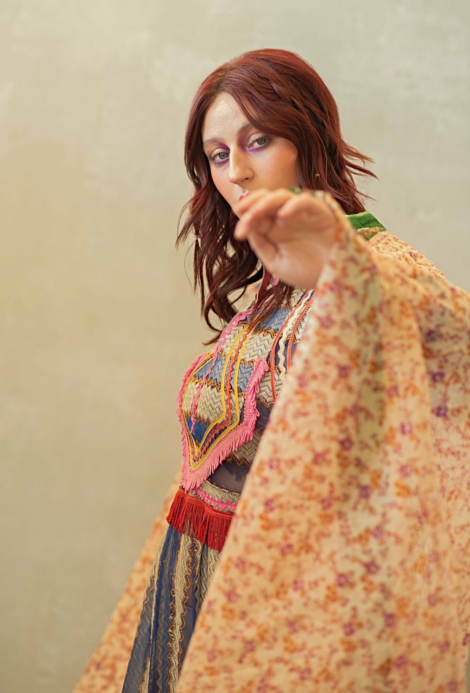 A woman in a floral dress is standing in front of a white wall.
