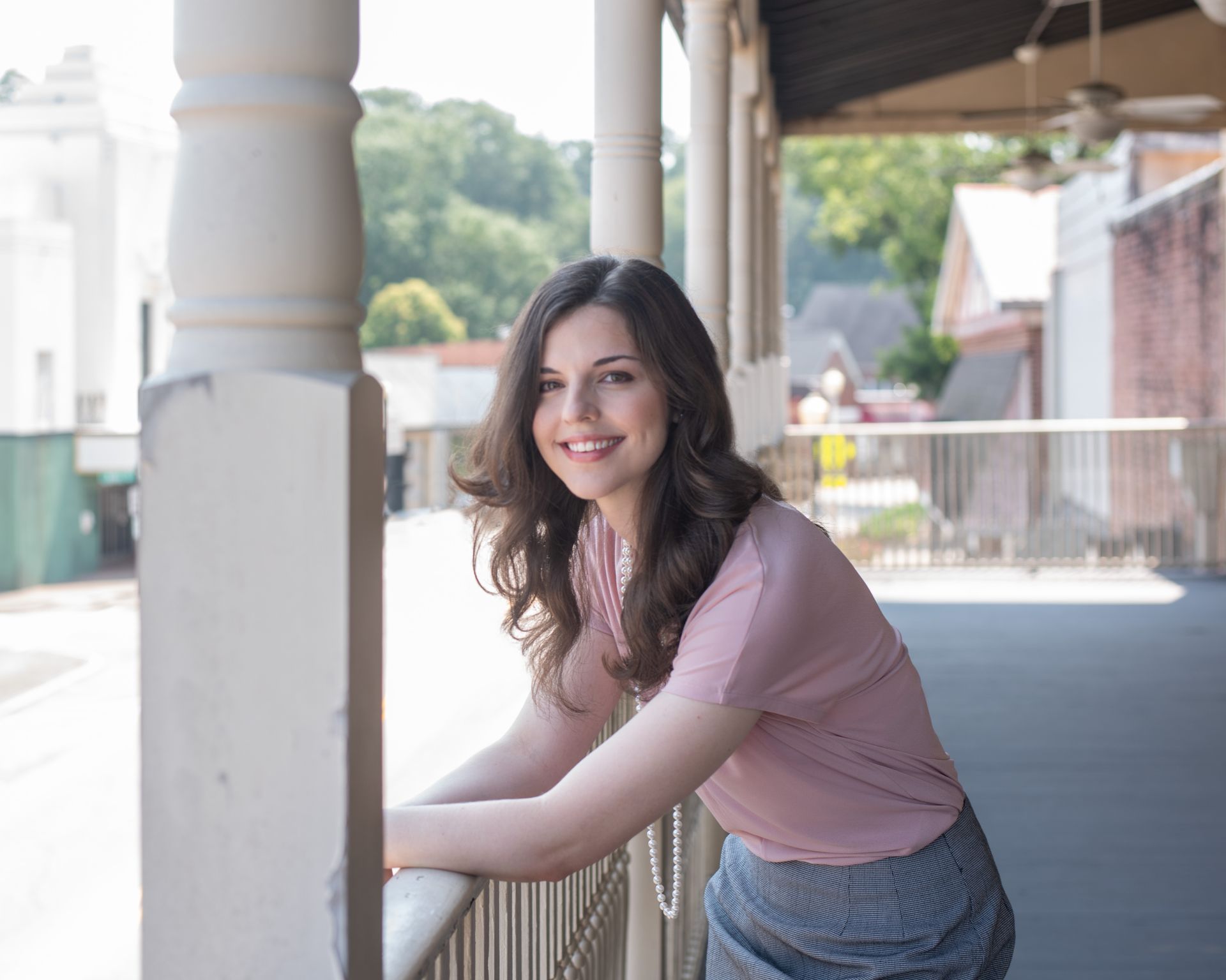 A woman is leaning on a railing on a porch and smiling.
