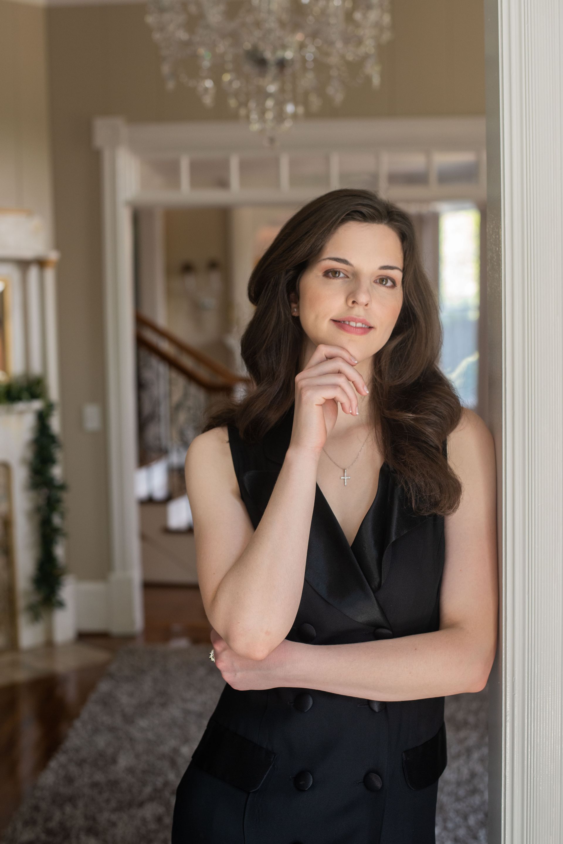 A woman in a black dress is leaning against a wall in a living room.