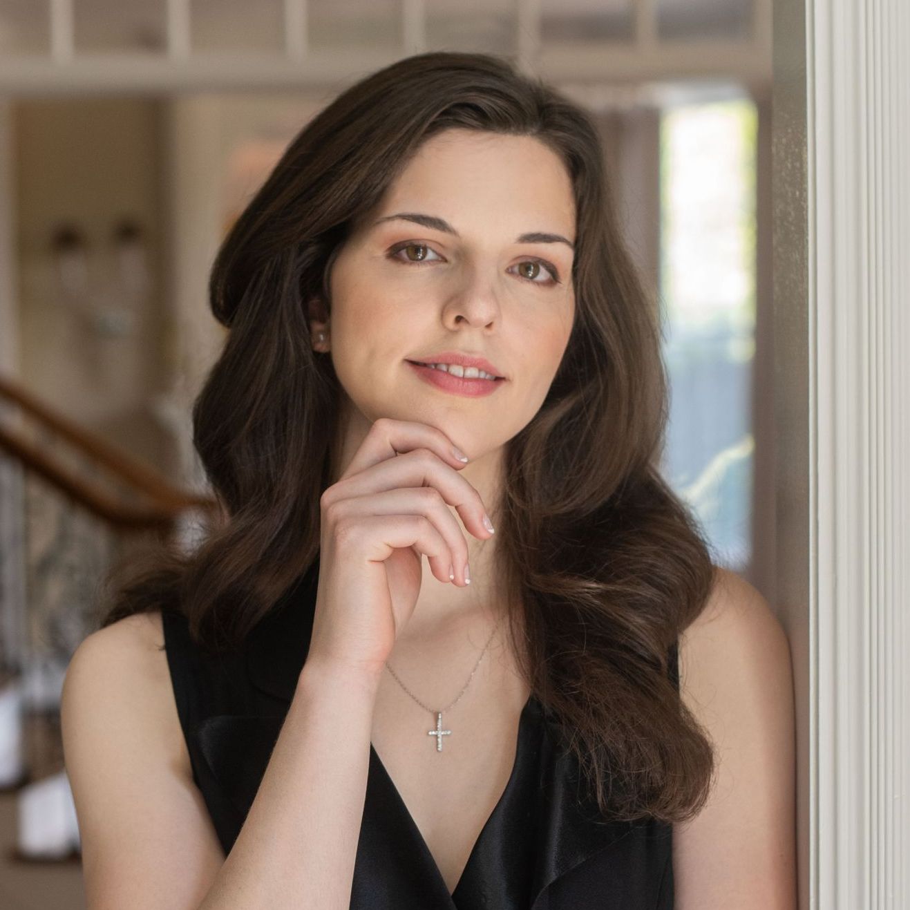 A woman is leaning against a wall with her hand on her chin.