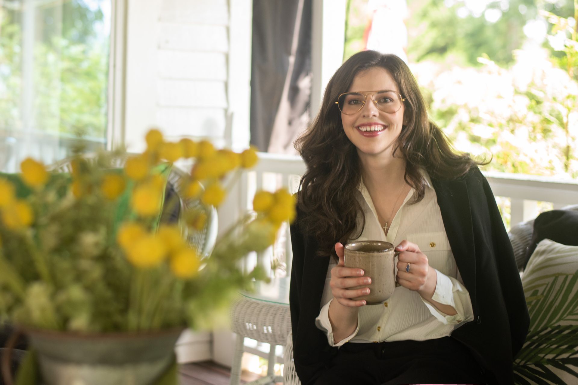 A woman is sitting on a porch holding a cup of coffee.