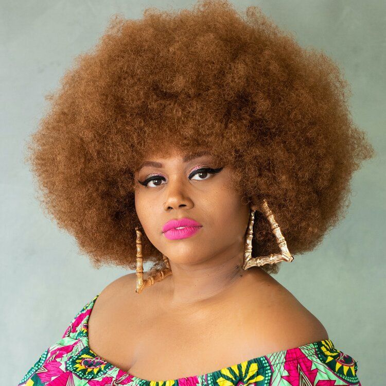 A woman with a large afro and earrings is wearing a colorful dress.