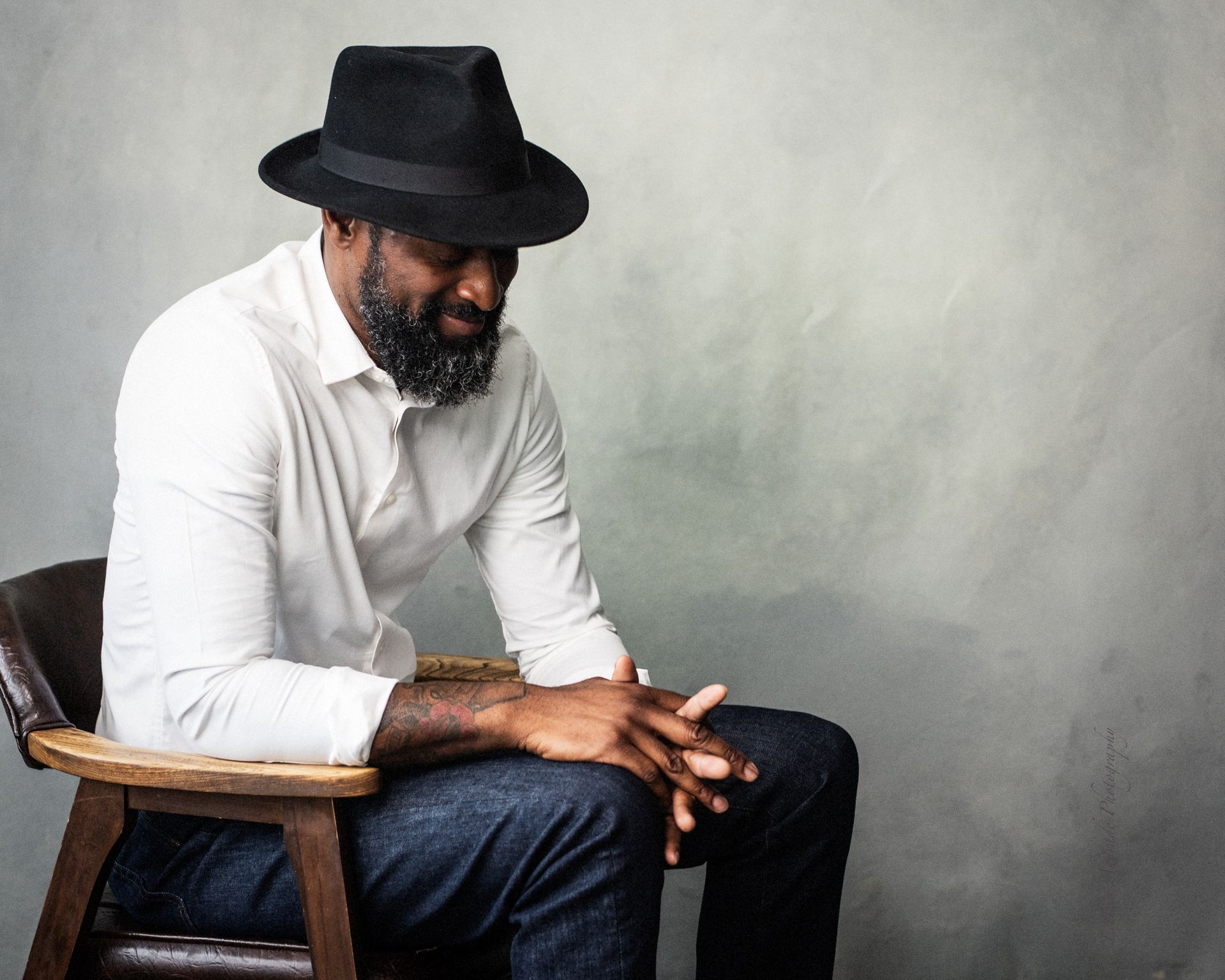 A man wearing a hat is sitting in a chair with his hands folded.