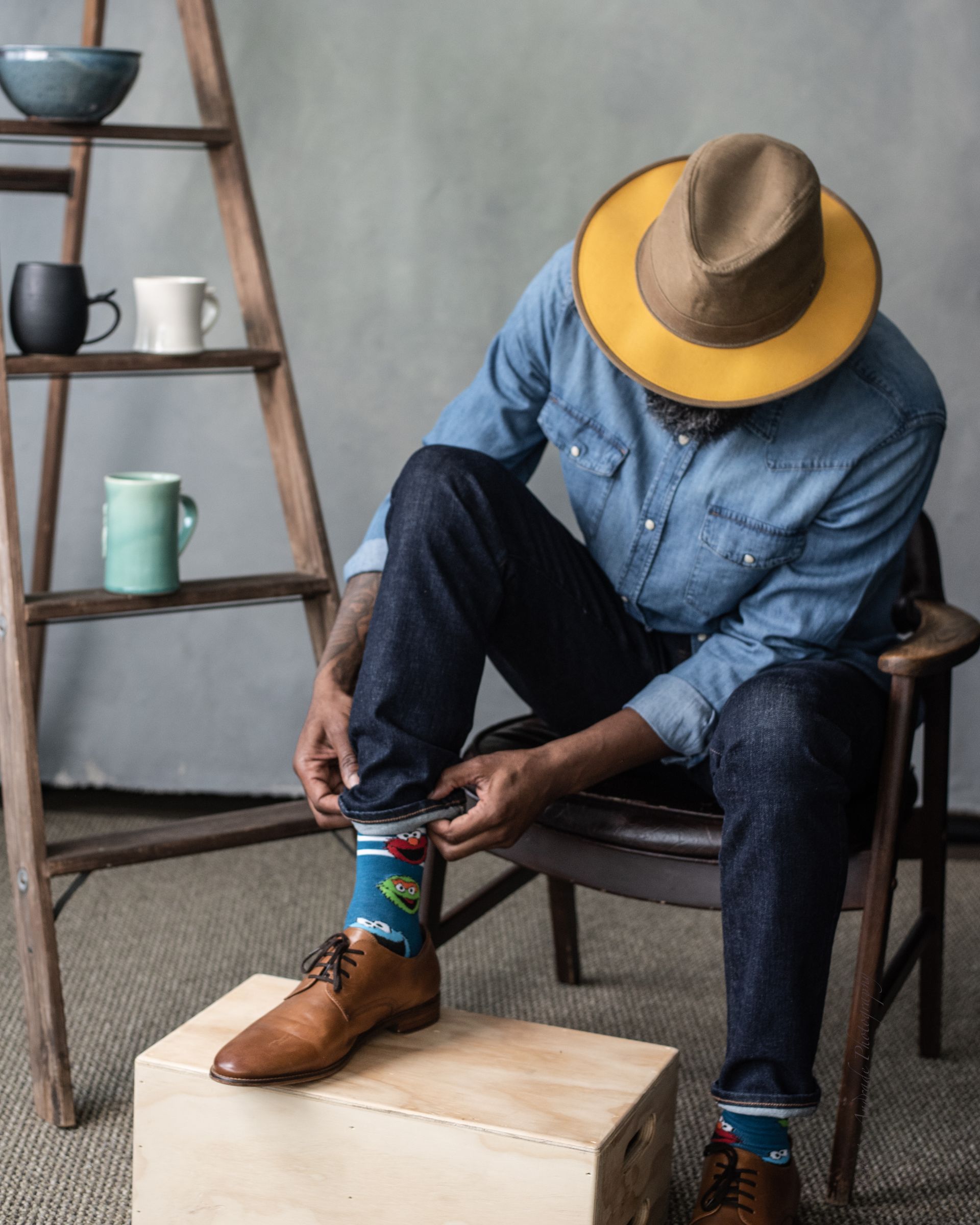 A man wearing a hat is tying his shoelaces while sitting in a chair.